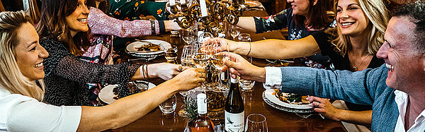 Personen sitzen bei einem gemütlichen Abend zusammen beim Essen am Tisch und prosten sich zu