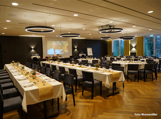 festlich gedeckte, lange Tafeln in Speisesaal mit Parkettboden